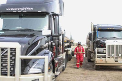Operations team member walking between commercial tanker trucks at a transportation yard, highlighting the coordination, safety, and efficiency of a professional operations team supporting liquid bulk transportation.